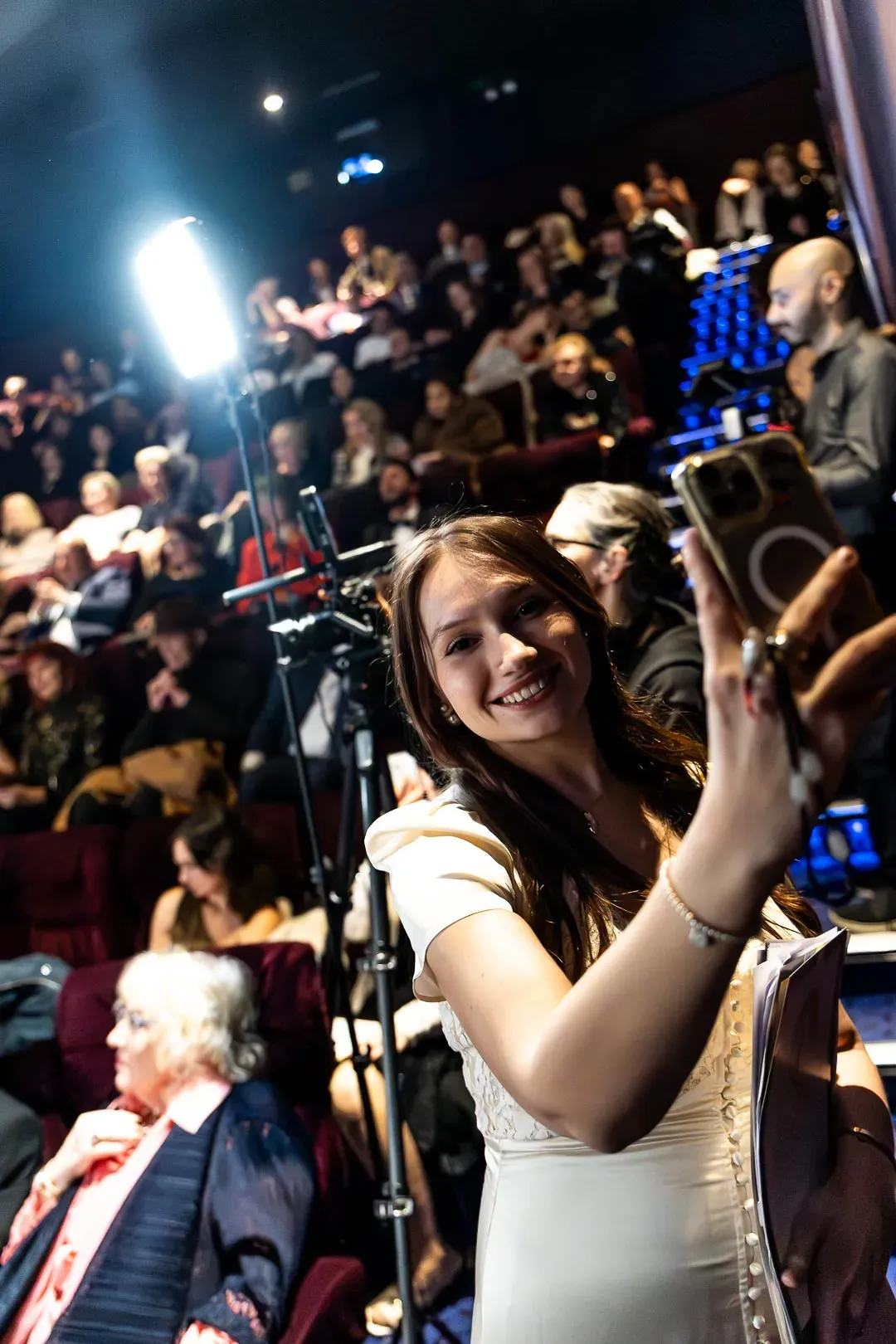 A young woman in a white dress takes a selfie in the cinema auditorium as guests take their seats at SIFFA 2025