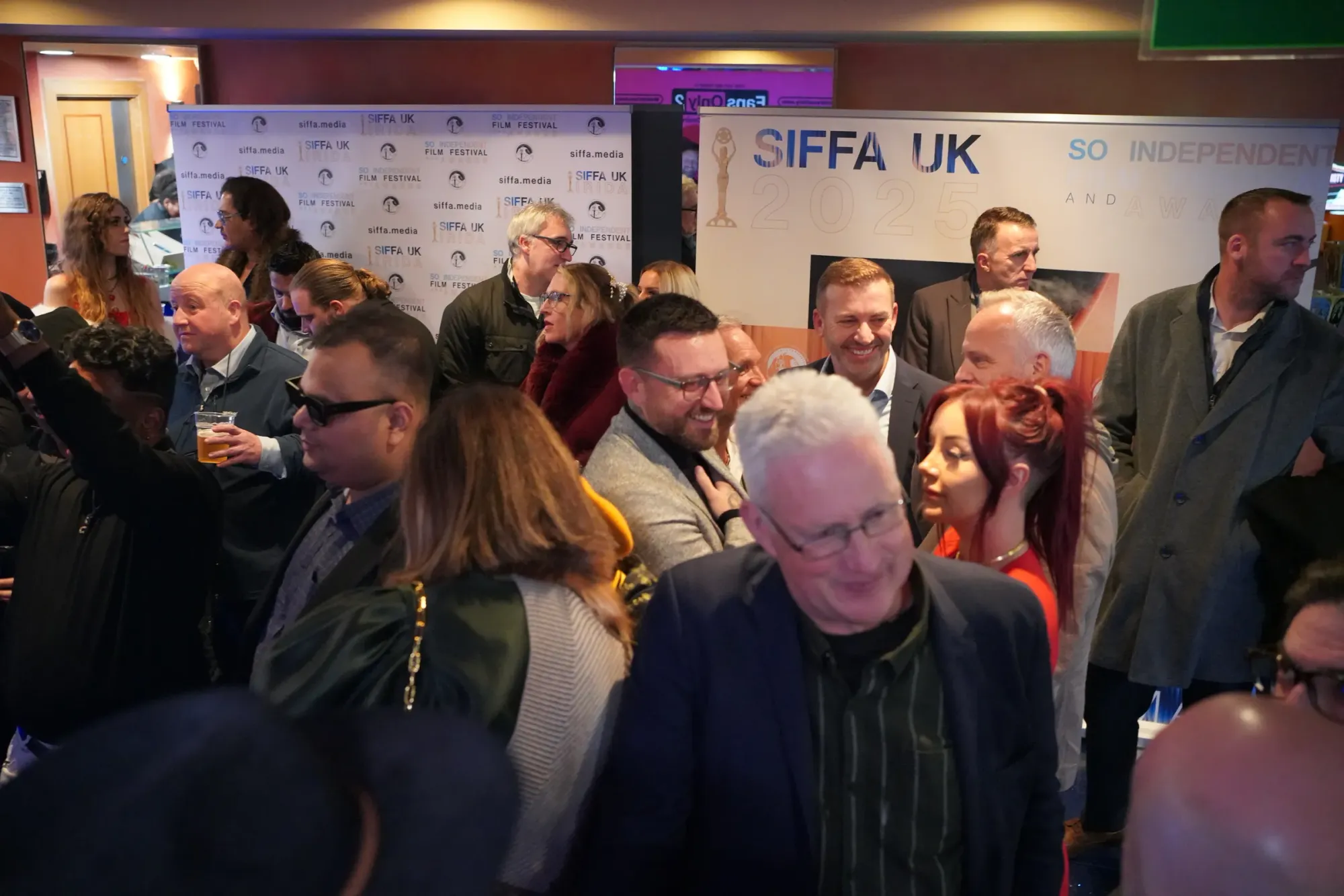 A crowd of guests mingling in the cinema foyer at SIFFA UK 2025, the branded festival backdrops behind them