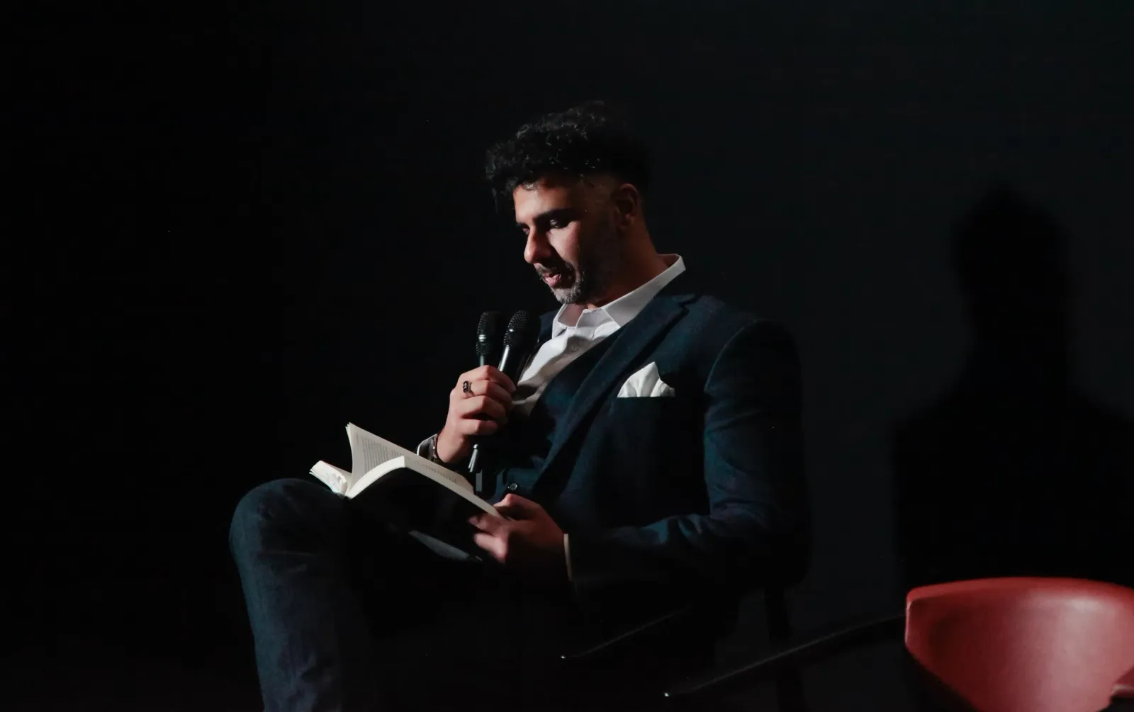 A man in a dark suit reads from a book into a microphone on stage at SIFFA 2024