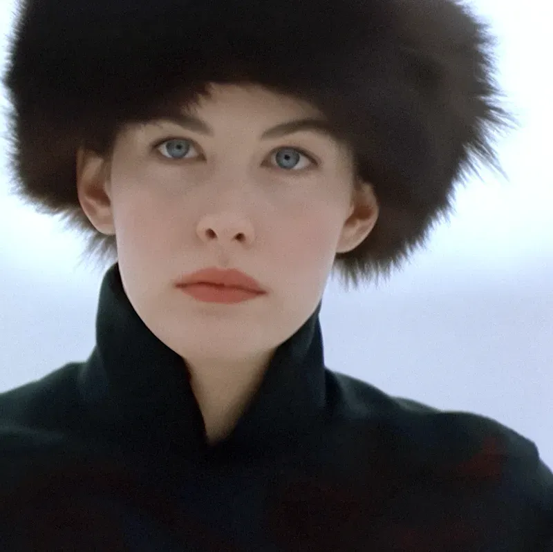 Film still: a woman in a dark fur hat and high-collared coat gazing at the camera against a pale wintry background